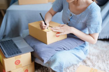 Bağımsız genç Asyalı kadın çevrimiçi satıcının küçük işletme girişimciliğine başlamak, bilgisayar kullanmak ve müşterilere dağıtım için ürünleri paketlemek için siparişler almaktır. KME dağıtım kavramı.