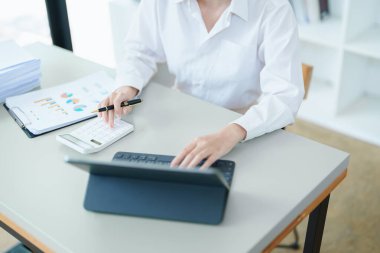 Düşünceli bir Asyalı iş kadınının portresi finansal tablolara bakıyor ve masasındaki bilgisayarı kullanarak pazarlama planları yapıyor..