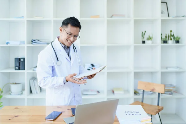 Portrait of a doctor looking at a patients information before treating a disease with using document and computer in work.