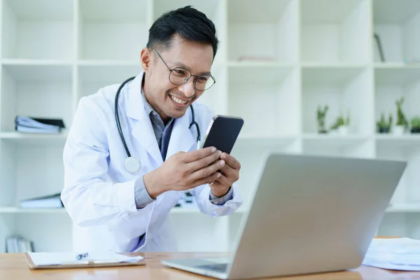Portrait of a doctor looking at a patients information before treating a disease with using smart phone and computer in work.