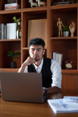 Masasında oturan yakışıklı ve ağzı sıkı Asyalı bir adamın portresi. Bilgisayarında düşünceli bir bakış var..