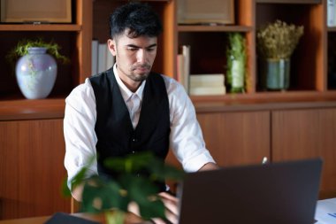 Masasında oturan yakışıklı ve ağzı sıkı Asyalı bir adamın portresi. Bilgisayarında düşünceli bir bakış var..