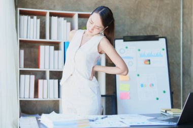 Uzun süre iş yerinde oturmaktan sırtı ağrıyan genç bir Asyalı kadının portresi.