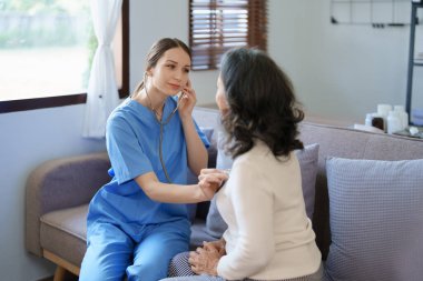 Yaşlı bir hastanın nabzını kontrol etmek için steteskop kullanan bir kadın doktorun portresi.