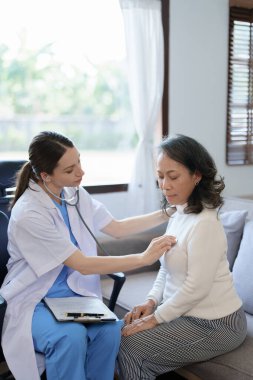 Yaşlı bir hastanın nabzını kontrol etmek için steteskop kullanan bir kadın doktorun portresi.