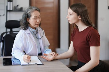 Yaşlı bir hastanın nabzını kontrol etmek için steteskop kullanan bir kadın doktorun portresi.