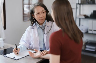 Yaşlı bir hastanın nabzını kontrol etmek için steteskop kullanan bir kadın doktorun portresi.