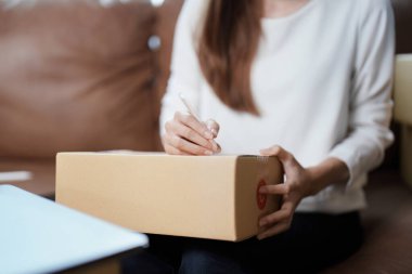 Bağımsız genç Asyalı kadın çevrimiçi satıcının küçük işletme girişimciliğine başlamak, bilgisayar kullanmak ve müşterilere dağıtım için ürünleri paketlemek için siparişler almaktır. KME dağıtım kavramı.