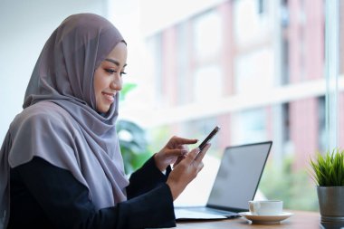 Güzel Müslüman kadın telefonda konuşuyor ve masasında bilgisayar kullanıyor..