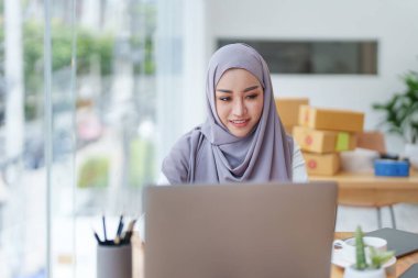 Müşteri siparişlerini, küçük işletme sahiplerini veya konseptleri kontrol etmek için bilgisayar kullanan güzel Müslüman kadın.