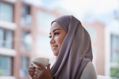 Sabahları gülümseyen bir yüzü olan, kahve içen ve bilgisayar kullanan güzel bir Müslüman kadın..