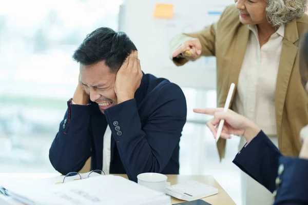 stock image An image of an Asian male employee looking worried and sad about being scolded by his boss for failing to meet sales targets, concept of disappointment and failure in his career.