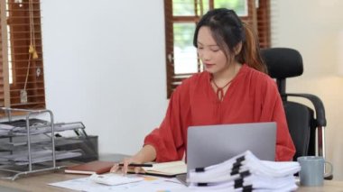 İş sahibi ya da Asyalı kadın pazarlamacılar evde hesap makinesi, defter ve bilgisayar kullanıyorlar. Yüksek kalite 4k görüntü