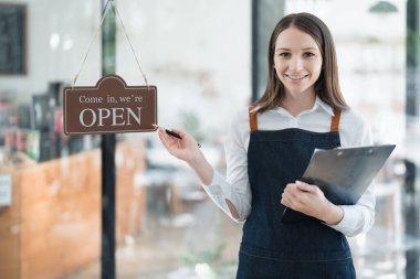 Küçük bir işletme kuran ve açan genç bir Asyalı kadın, kafeterya tezgahının önünde duran önlüklü gülen bir yüz gösteriyor. İş sahibi, Restoran, Barista, Cafe, Çevrimiçi KOBİ.