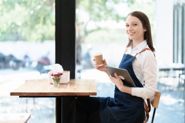Küçük bir işletme kuran ve açan genç bir Asyalı kadın, kafeterya tezgahının önünde duran önlüklü gülen bir yüz gösteriyor. İş sahibi, Restoran, Barista, Cafe, Çevrimiçi KOBİ.
