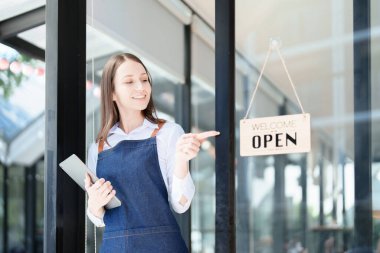 Küçük bir işletme kuran ve açan genç bir Asyalı kadın, kafeterya tezgahının önünde duran önlüklü gülen bir yüz gösteriyor. İş sahibi, Restoran, Barista, Cafe, Çevrimiçi KOBİ.