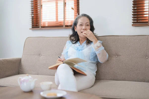 stock image Portrait of an elderly Asian woman holding a notebook eating snacks and drinking tea