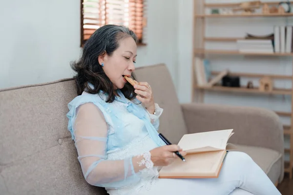 stock image Portrait of an elderly Asian woman holding a notebook eating snacks and drinking tea