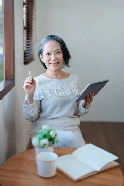 Portrait of an elderly Asian woman in a modern pose working on a tablet computer