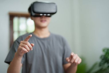 Evde sanal gerçeklik simülatörü kulaklığı kullanan Asyalı genç bir adamın portresi.