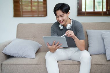 Rahatlarken gülümseyen bir adamın portresi, müzik dinlemek için bir tablet bilgisayar ve kulaklık kullanıyor..