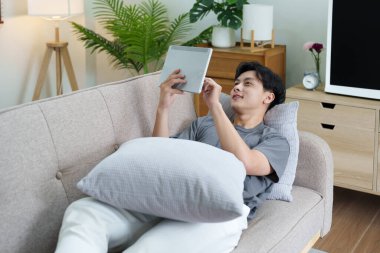 Evde dinlenirken dijital tablet kullanan Asyalı bir gencin portresi..