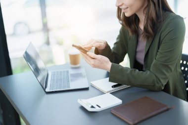 Portrait of a young Asian man showing a smiling face as she uses his phone, computer and financial documents on her desk in the early morning hours.