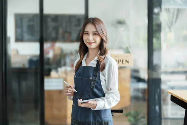 open a small business Portrait of happy Asian woman in apron holding tablet in front of cafe