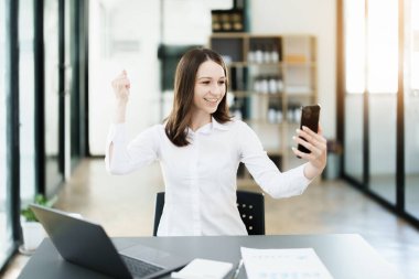 Ofisteyken cep telefonu kullanan heyecanlı bir iş kadını