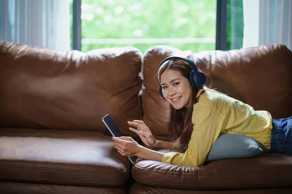 亚洲女人在家里沙发上使用平板电脑和耳机放松的肖像 — 图库照片