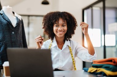 Mutlu bir gülümseme genç Afro-Amerikan moda tasarımcısı başarılı bir moda stüdyosunda çalışan bilgisayar laptopu kullanıyor..