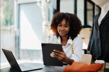 Genç Afro-Amerikan ve Asyalı kadın moda tasarımcısı moda stüdyosunda çalışıyor..