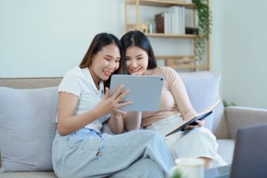 Igbtq, Igbt konsepti, homoseksüellik, iki Asyalı kadının birlikte mutlu poz vermeleri ve kanepede tablet oynarken birbirlerini sevmeleri..