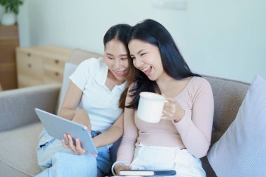 Igbtq, Igbt konsepti, homoseksüellik, iki Asyalı kadının birlikte mutlu poz vermeleri ve kanepede tablet oynarken birbirlerini sevmeleri..