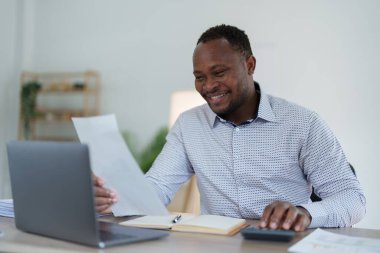 Orta yaşlı Amerikalı Afrikalı adam hesaplama ve dizüstü bilgisayarı kullanarak finansal belge, vergi, döviz, muhasebe ve mali danışman üzerinde çalışıyor..