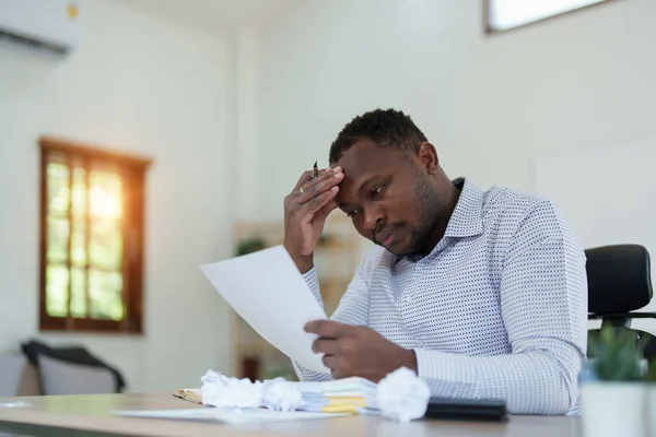 Burnout American African business man in stress works with many paperwork document, migraine attack, Freelance, work from home.