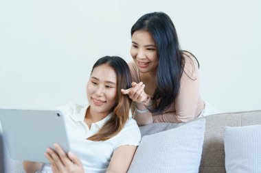 Igbtq, Igbt konsepti, homoseksüellik, iki Asyalı kadının birlikte mutlu poz vermeleri ve kanepede tablet oynarken birbirlerini sevmeleri..