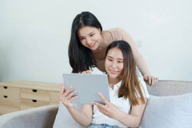 Igbtq, Igbt konsepti, homoseksüellik, iki Asyalı kadının birlikte mutlu poz vermeleri ve kanepede tablet oynarken birbirlerini sevmeleri..