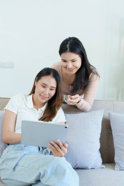 Igbtq, Igbt konsepti, homoseksüellik, iki Asyalı kadının birlikte mutlu poz vermeleri ve kanepede tablet oynarken birbirlerini sevmeleri..