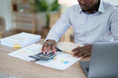 Orta yaşlı Amerikalı Afrikalı adam hesaplama ve dizüstü bilgisayarı kullanarak finansal belge, vergi, döviz, muhasebe ve mali danışman üzerinde çalışıyor..