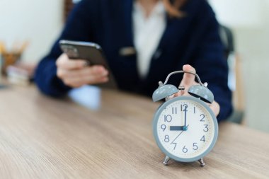 Masadaki çalar saat. Modern ofis binasında ya da gece çalışan Asyalı iş kadını ofisteki akıllı telefonu kullanıyor..