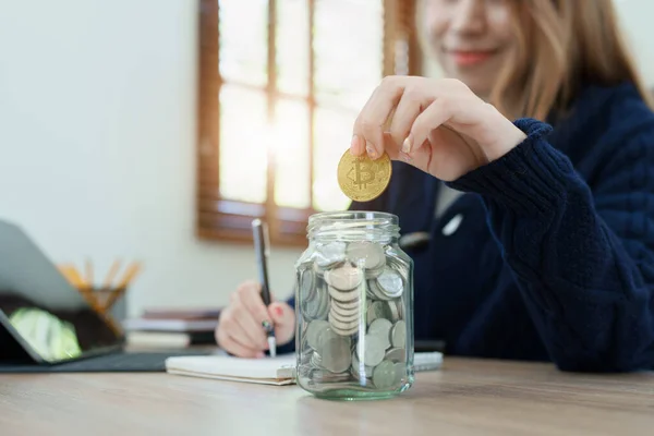 Cryptocurrency savings plan, Asian young woman saving digital coins into a piggy bank.