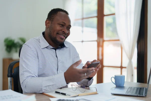 Orta yaşlı Amerikalı Afrikalı adam akıllı telefon ve dizüstü bilgisayar kullanarak finansal belge, vergi, döviz, muhasebe ve mali danışman üzerinde çalışıyor..