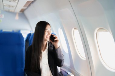 Asyalı iş kadını yolcu akıllı telefon konuşmaları ya da video konferans ve seyahat konseptini kullanarak çalışırken birinci sınıf lüks uçakta oturuyor..