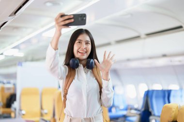Asyalı iş kadını yolcu akıllı telefon konuşmaları ya da video konferans ve seyahat konseptini kullanarak çalışırken birinci sınıf lüks uçakta oturuyor..