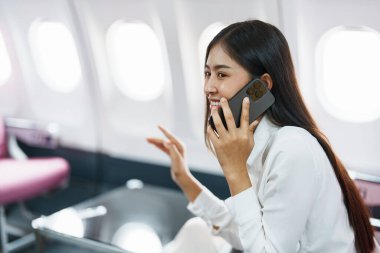 Asyalı iş kadını yolcu akıllı telefon konuşmaları ya da video konferans ve seyahat konseptini kullanarak çalışırken birinci sınıf lüks uçakta oturuyor..