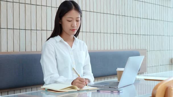 Młoda Azjatka Pracująca Komputerze Trzymająca Długopis Notatek Notatniku Kawiarni Wysokiej — Wideo stockowe