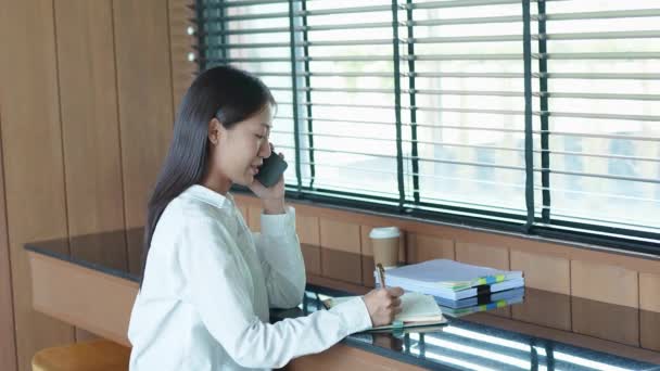 Молодая Азиатка Использующая Смартфон Разговаривает Телефону Делает Заметки Блокноте Кафе — стоковое видео