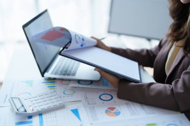 Ofisteki muhasebe belgesini kullanırken iş verilerini hesaplamak için hesap makinesi ve dizüstü bilgisayar üzerinde çalışan iş kadını veya muhasebeci.