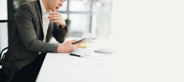 Portrait of a young Asian man showing a smiling face as she uses his phone, computer and financial documents on her desk in the early morning hours.